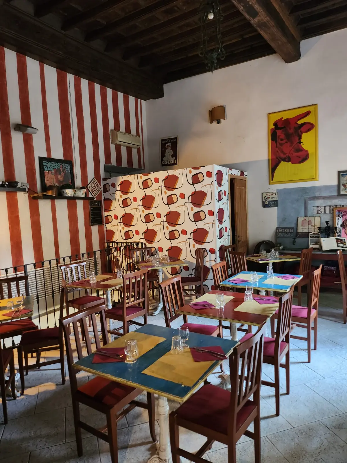 The dining room: red and white striped walls, yellow and blue tables, wooden beams